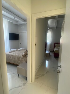 A hotel room with a bed, a desk, a chair, a TV, and a bathroom with a red chair.