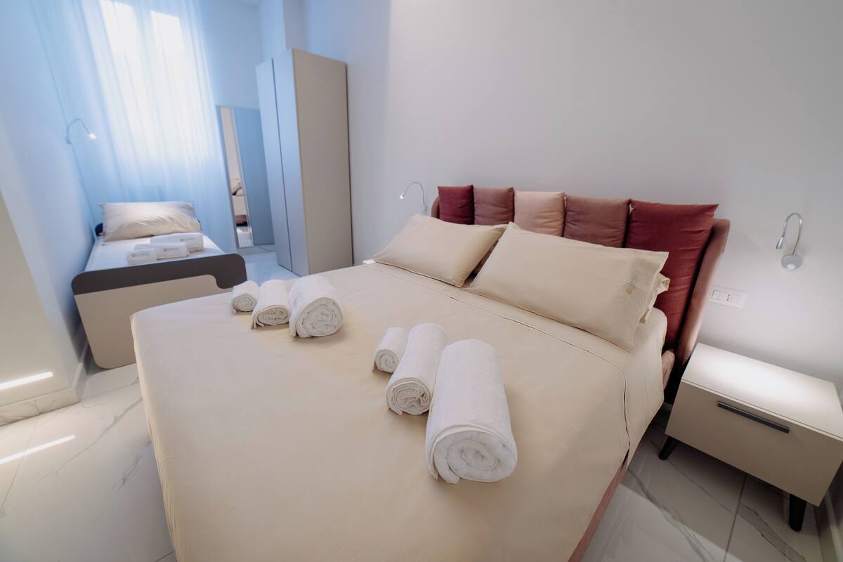A hotel room with a bed, a nightstand, a mirror, and a window with curtains.