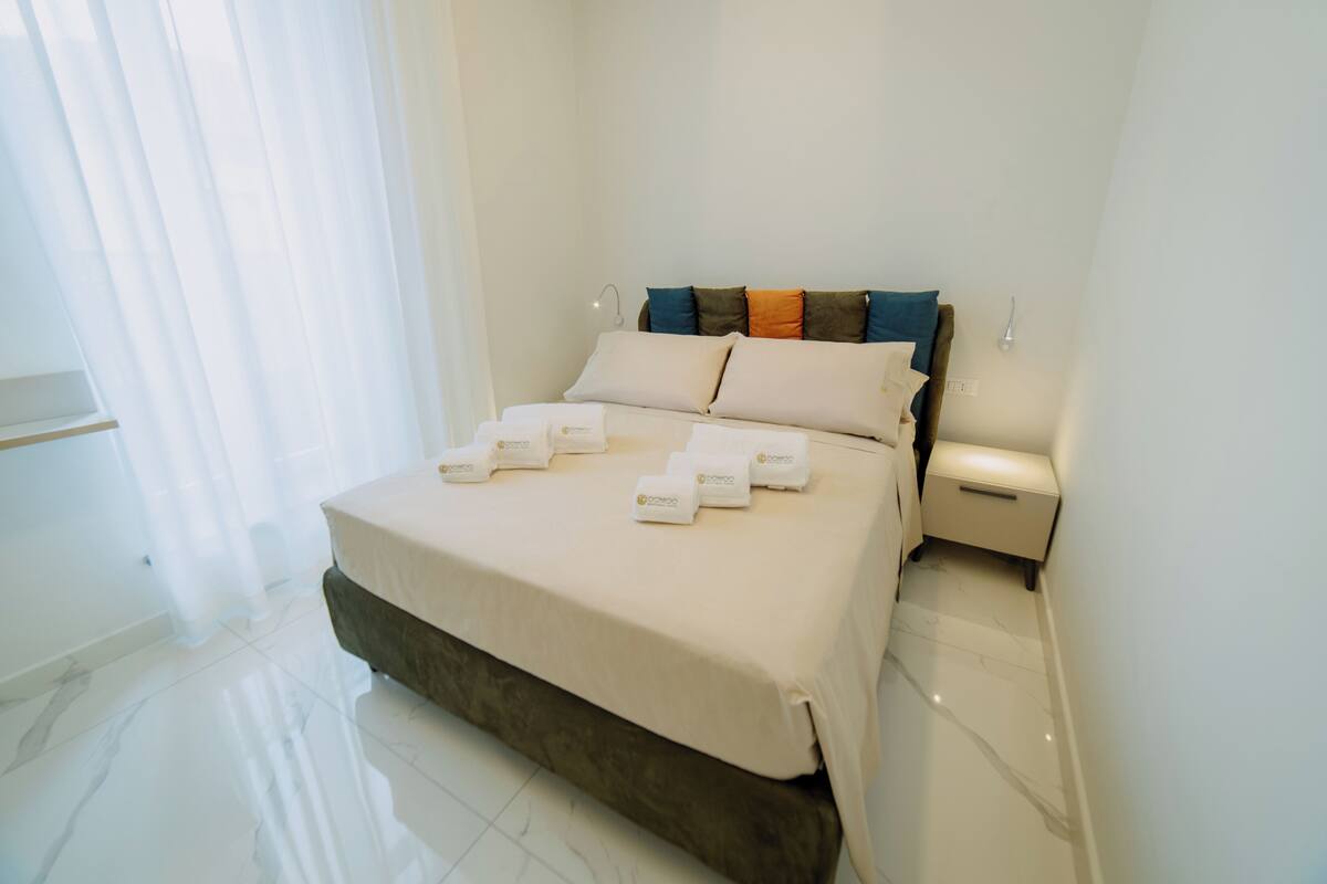 A hotel room with a bed, bedside tables, and a window with curtains.