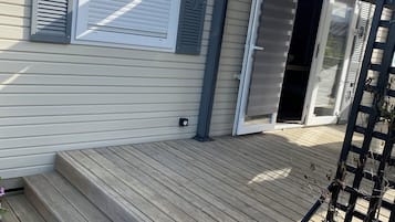Une terrasse en bois menant à une maison dotée d’une porte-fenêtre coulissante et d’un patio couvert.