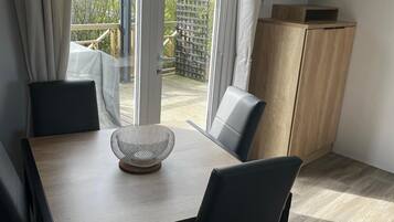 Un coin repas comprenant une table, des chaises, un téléviseur posé sur un meuble et une vue à travers une porte vitrée.