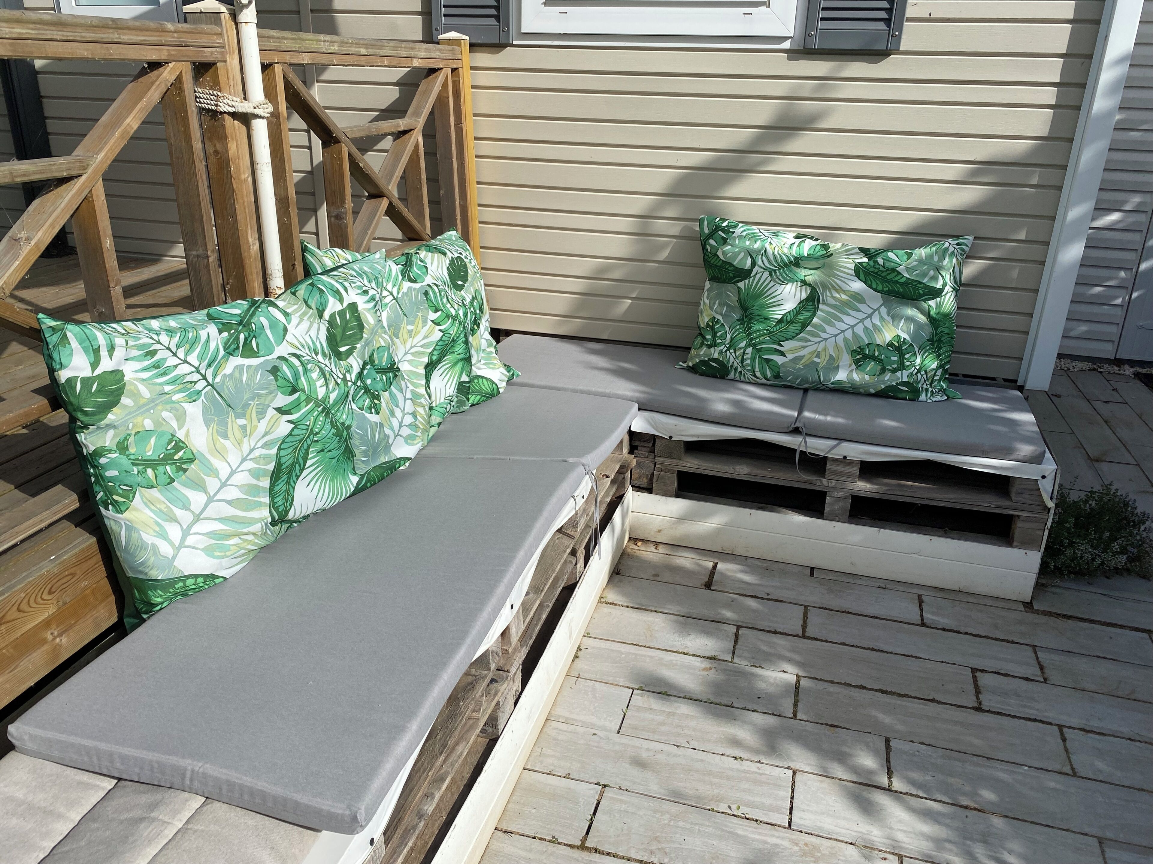 Eine Holzterrasse mit integriertem Sitzplatz und Kissen mit Blattmuster.