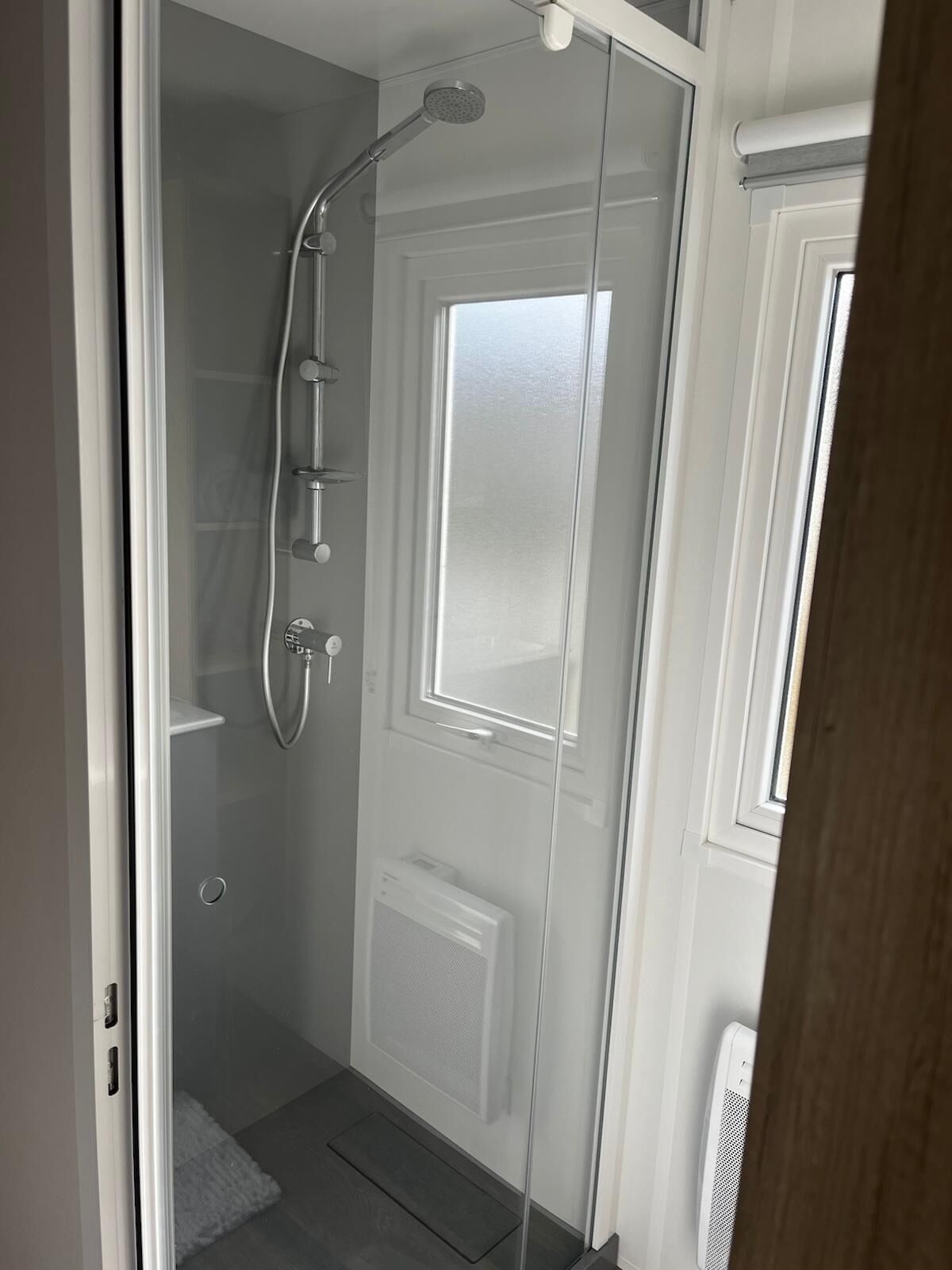 Une douche à l’italienne avec une porte en verre, une fenêtre et un radiateur.