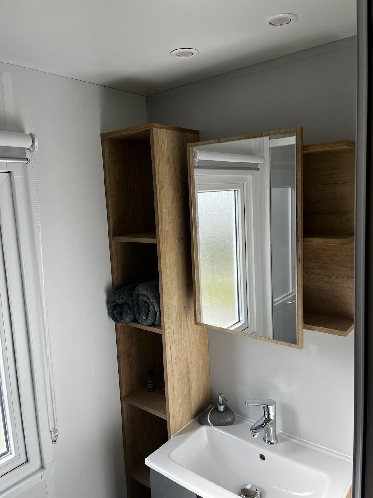 Une salle de bain avec un lavabo blanc, un miroir, des étagères en bois et un porte-serviettes.