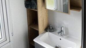 A bathroom with a white sink, a mirror, wooden shelves, and a towel rack. - Mobile home at a 2-star campground, a 10-minute walk from the beach (Saint-Cast-le-Guildo)