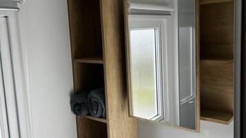 Une salle de bain avec un lavabo blanc, un miroir, des étagères en bois et un porte-serviettes.