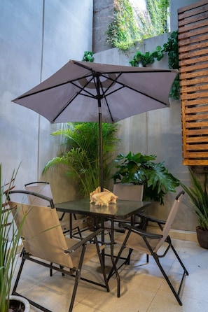 Eine Terrasse mit Tisch und Stühlen, einem großen Sonnenschirm und verschiedenen Kübelpflanzen.