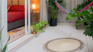 Une terrasse moderne agrémentée d’un hamac, de plantes en pot et d’une œuvre d’art colorée accrochée au mur.