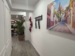 Ein Flur mit einem Blumentopf, einem Kleiderständer und einem großen Gemälde einer Straßenszene.