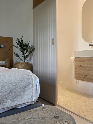 A bedroom with a bed, a bedside table, a mirror, a potted plant, and a door.