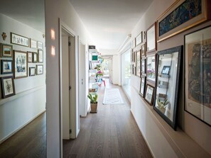 Ein Korridor mit gerahmten Kunstwerken an den Wänden, einem Blumentopf und Holzboden.