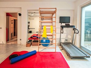 Ein Heimfitnessraum mit Klimmzugstange, Übungsball, Laufband und Yogamatten.