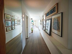 A hallway with framed artwork on the walls, wooden flooring, and a potted plant. - Mulberry Garden by Interhome (Belvedere Ostrense)