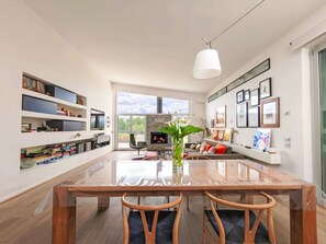 Ein modernes Wohnzimmer mit einem Holzespeisetisch, Stühlen, einem Kamin und einem großen Fenster.