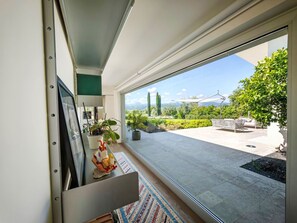 Ein modernes Zimmer mit einer großen Schiebetür, die auf eine Außenveranda mit Blick auf Grünflächen und ferne Berge führt.