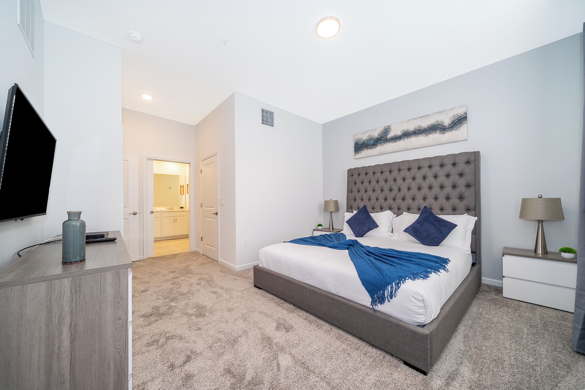 A bedroom with a large bed, bedside tables, a flat-screen TV, and a door leading to a bathroom.