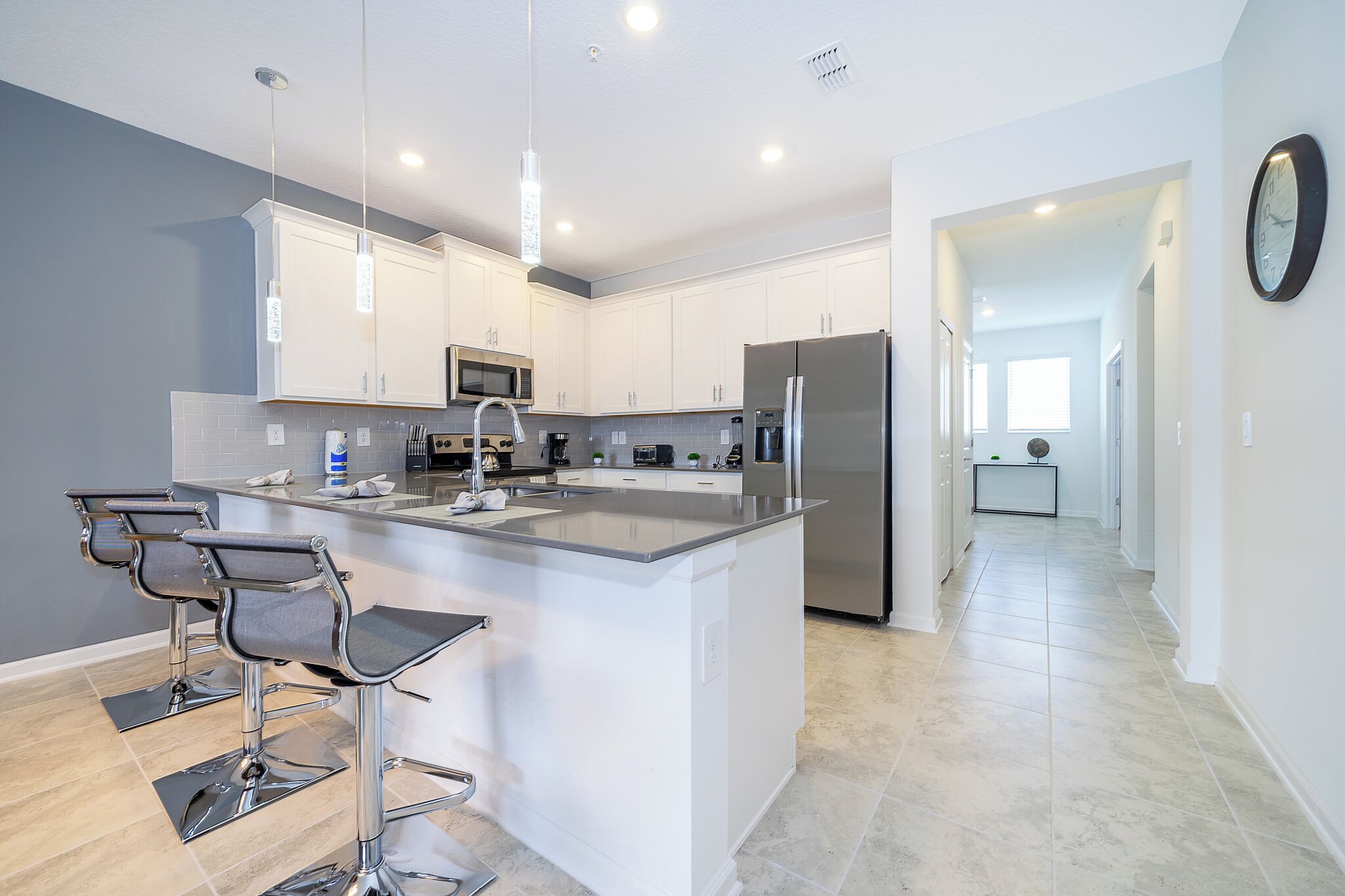 Una cocina moderna con armarios blancos, electrodomésticos de acero inoxidable y una isla central con taburetes de bar.