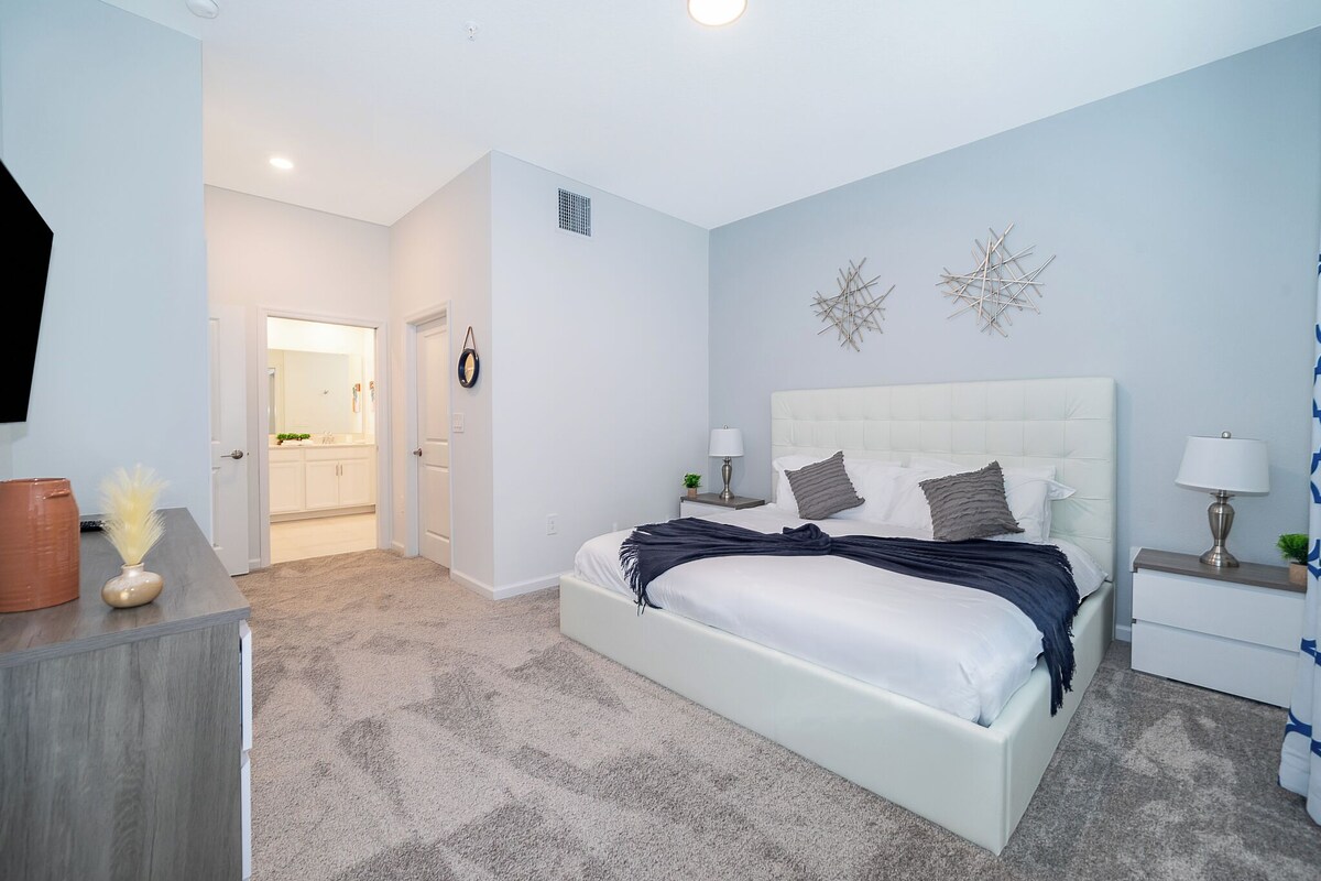 A bedroom with a large bed, bedside tables, a nightstand, and a door leading to a bathroom.