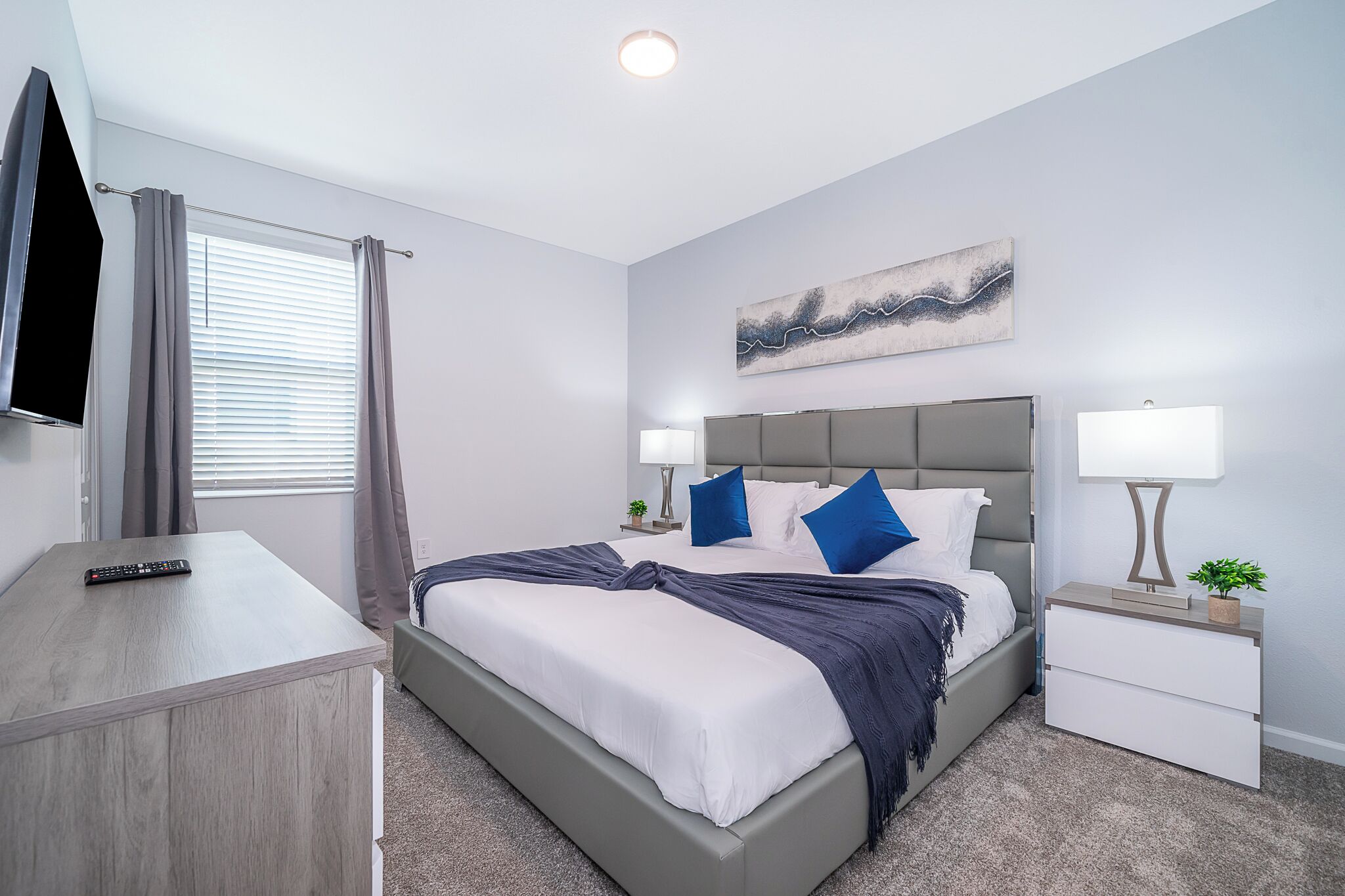 A modern bedroom with a bed, bedside tables, a TV, and a painting on the wall.