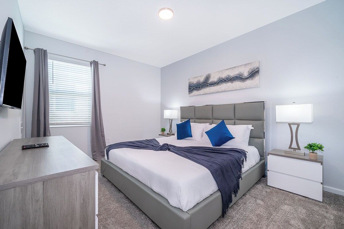 A modern bedroom with a bed, bedside tables, a TV, and a painting on the wall.