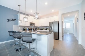 A modern kitchen with white cabinets, stainless steel appliances, and a bar area with stools. - AEA - Davenport FL  (Kissimmee)