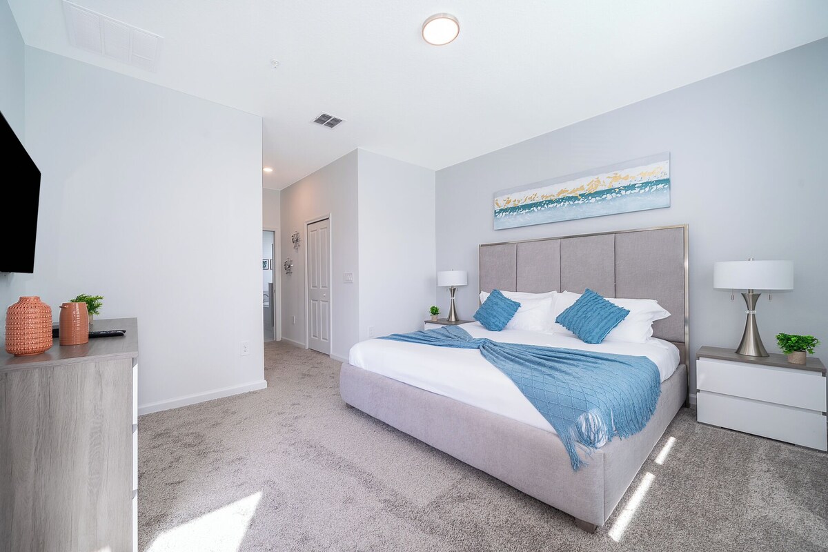 A modern bedroom with a large bed, bedside tables, a desk, and a wall-mounted artwork.