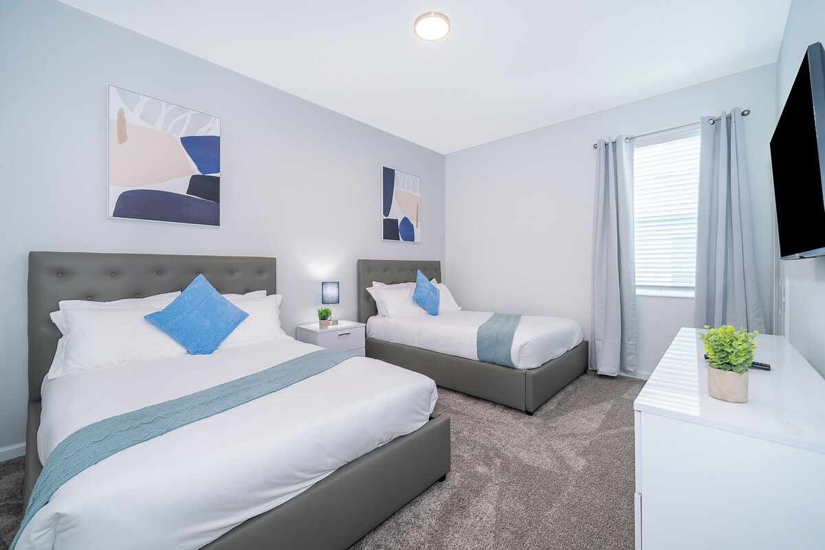 A modern hotel room with two beds, a desk, and a TV.