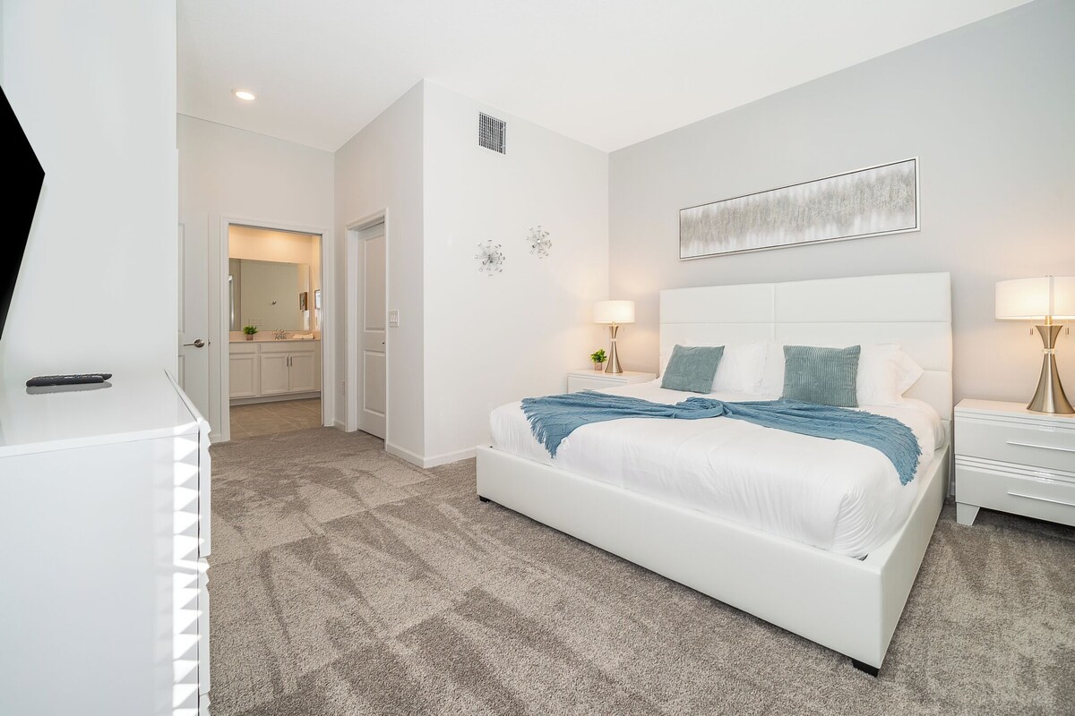 A modern bedroom with a white bed, bedside tables, and a hallway leading to a bathroom.
