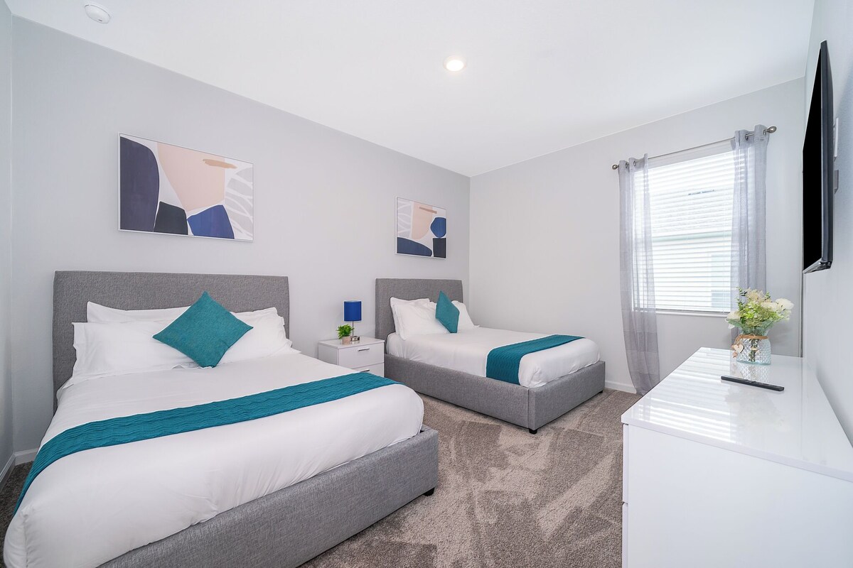 A hotel room with two beds, a desk, and a TV.