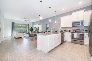 A modern kitchen with white cabinetry, a large island, stainless steel appliances, and pendant lighting. - AEA - Davenport FL  (Kissimmee)