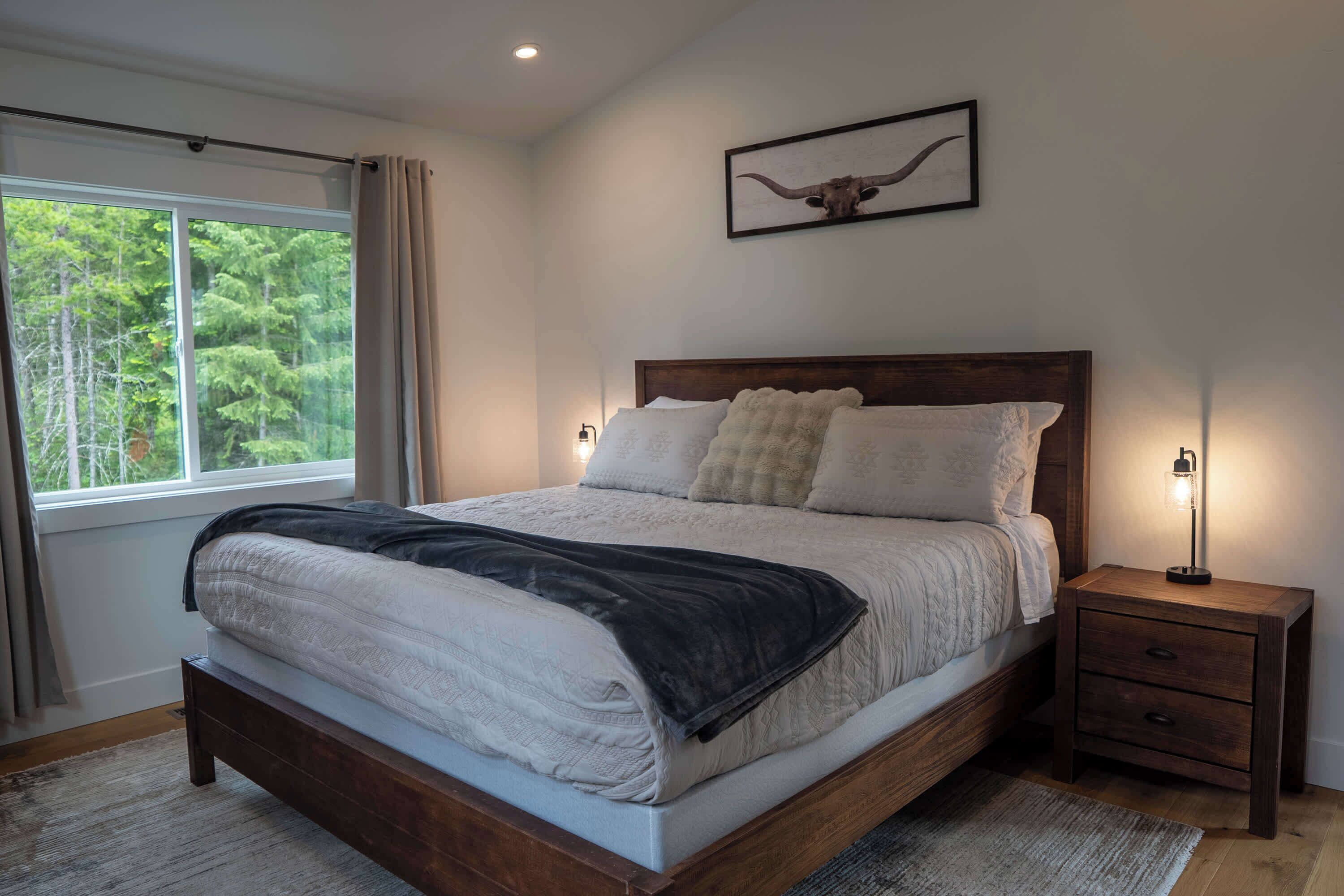 Une chambre à coucher avec un grand lit, une table de chevet avec une lampe, un tableau encadré au mur et une fenêtre avec des rideaux.