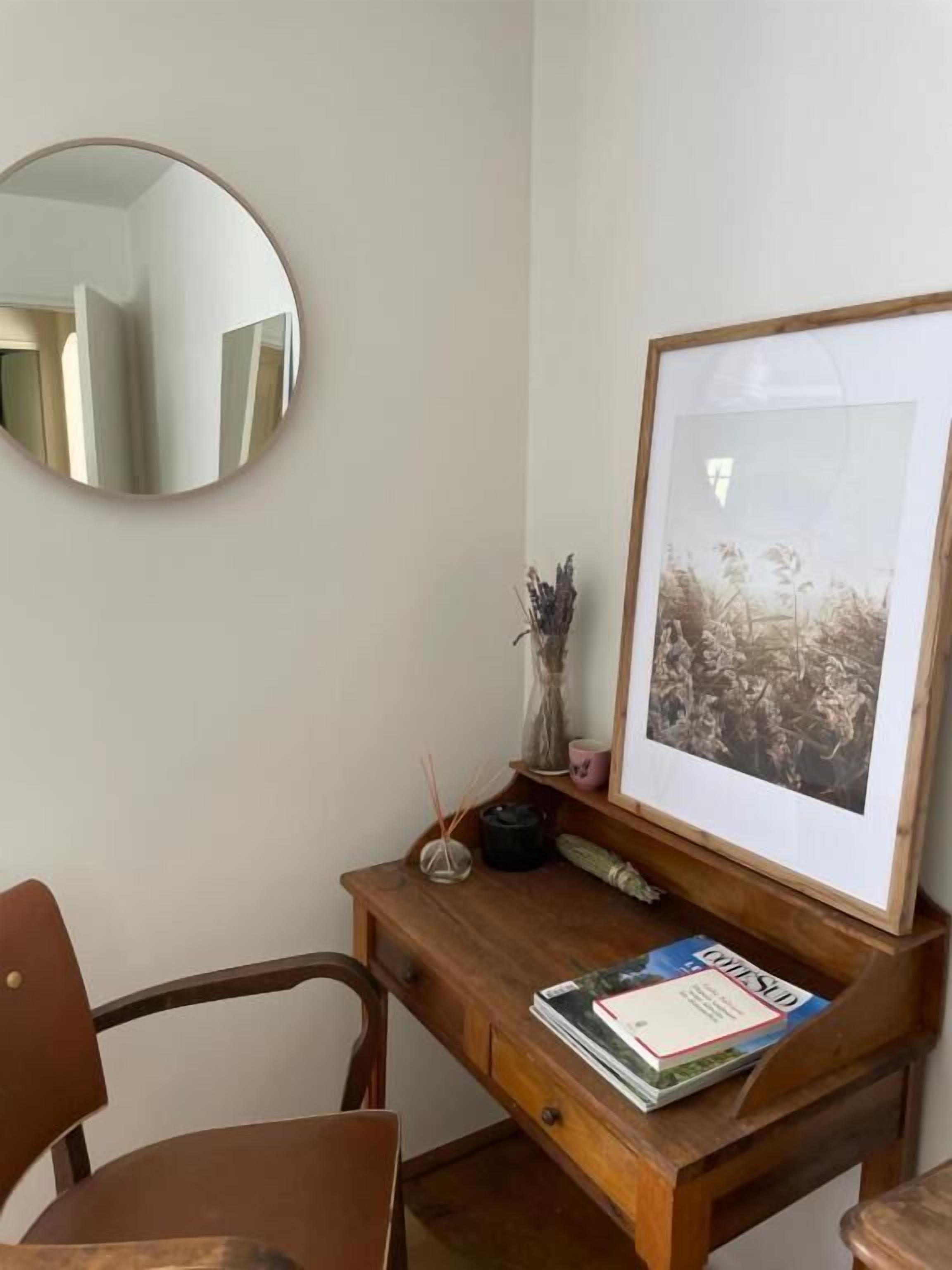 Een houten bureau met een lijstfoto, een spiegel en een stoel.