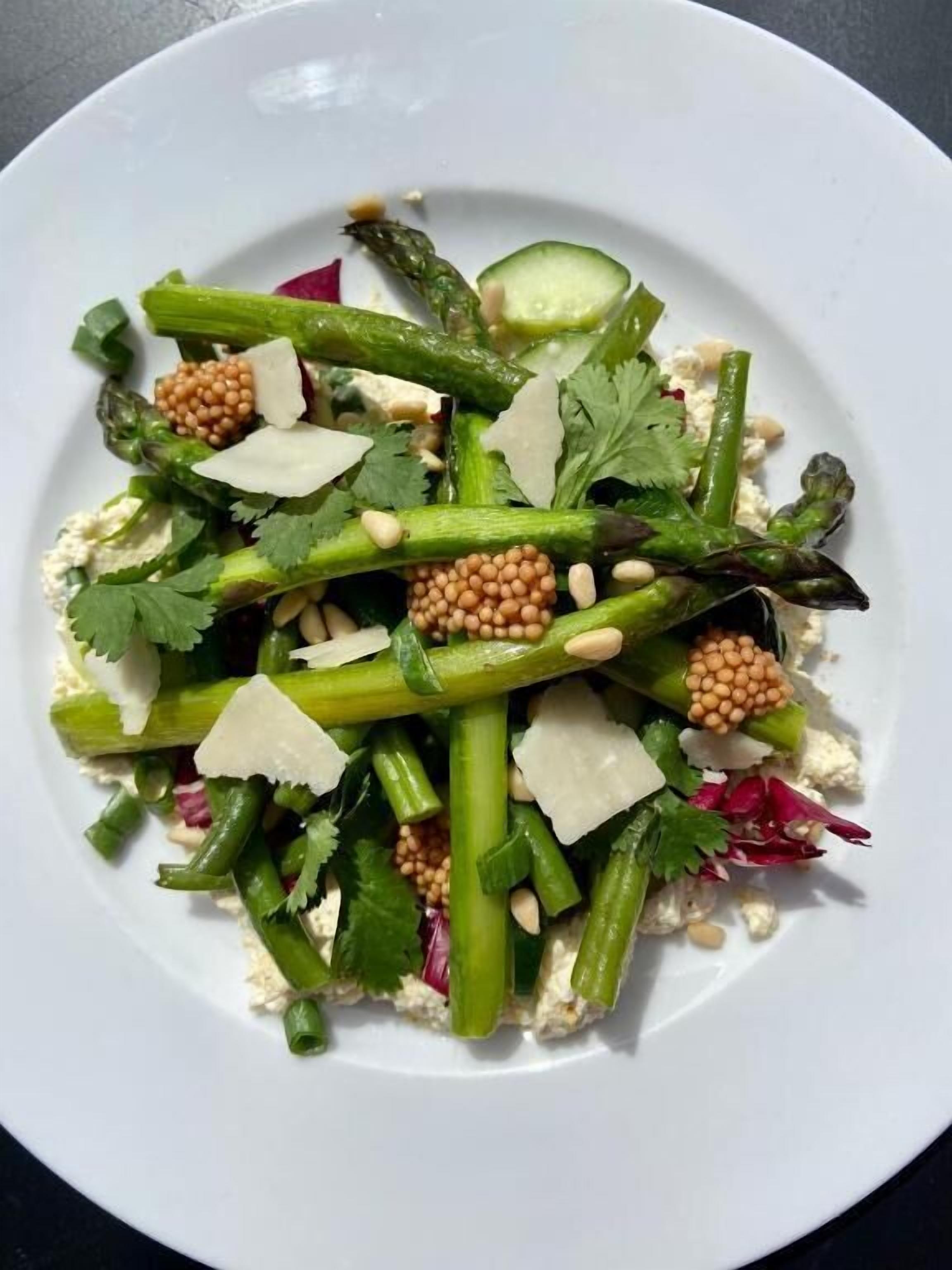 Une assiette blanche contenant une salade composée de légumes verts, de fromage et de pignons de pin.