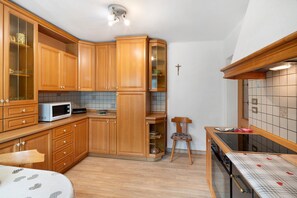 A compact kitchen with wooden cabinets, a microwave, and a small dining table with a chair. - Apartment 'Roda De Vael' with Mountain View, Balcony and Wi-Fi (Vigo di Fassa)