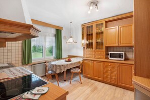 A kitchen with wooden cabinets, a dining table with chairs, a microwave, and a window with curtains. - Apartment 'Roda De Vael' with Mountain View, Balcony and Wi-Fi (Vigo di Fassa)