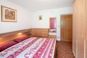 A bedroom with a bed, a nightstand, a dresser, a mirror, and a door. - Apartment 'Roda De Vael' with Mountain View, Balcony and Wi-Fi (Vigo di Fassa)