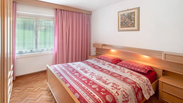Un dormitorio con cama, una ventana con cortinas, una mesita de noche y un cuadro colgado en la pared.