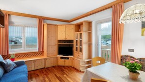 Una habitación acogedora con un armario de madera, un televisor, una mesa de comedor y una ventana con cortinas.