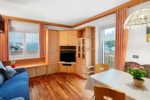 Ein gemütliches Zimmer mit Holzschrank, Fernseher, Esstisch und einem blickdichten Fenster.