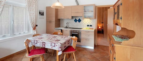 A compact kitchen with wooden cabinets, a dining table with chairs, and a hanging light fixture.