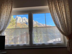 A room with a large window featuring a mountain view, sheer curtains, and a textured window blind. - Apartment 'Cima Dodici' with Mountain View and Wi-Fi (Vigo di Fassa)