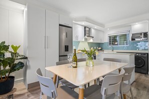 A modern kitchen with white cabinets, a stainless steel refrigerator, a built-in oven, and a washing machine. - Ocean View C303 (Cape Town)