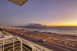 A coastal road with vehicles, a beach, and a mountain in the distance. - Ocean View C303 (Cape Town)