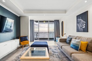 A modern living room with a sofa, ottoman, and a flat-screen TV. - Ocean View C303 (Cape Town)