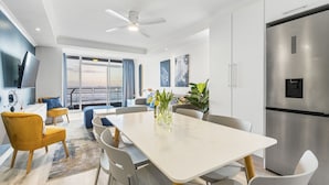 A modern kitchen with a stainless steel refrigerator, a dining area with a white table and chairs, and a large window with a view. - Ocean View C303 (Cape Town)