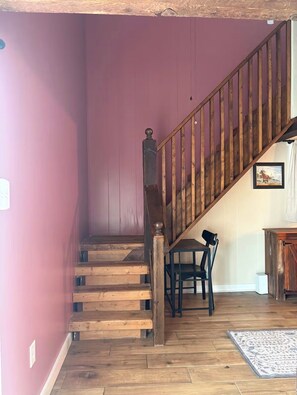 Un escalier en bois avec une rampe, une chaise et un tapis sur un plancher en bois.