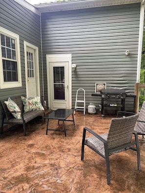 Une terrasse couverte avec une table, des chaises, un banc et un barbecue.