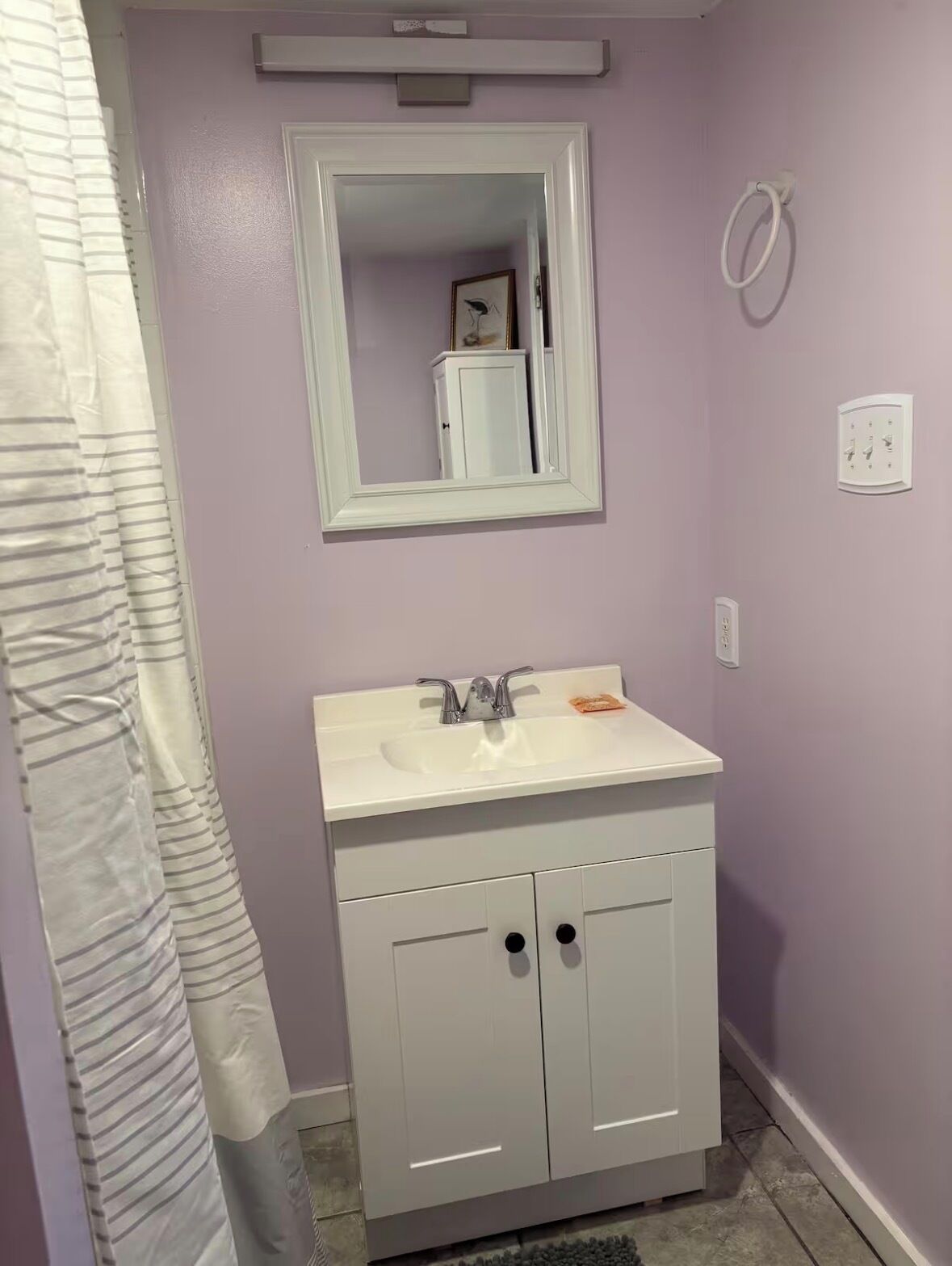 A bathroom with a white sink, mirror, and cabinet, a shower curtain, and a towel rack.