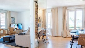 A modern living room with a sofa, dining table, chairs, and a TV. - Les Balmettes I T3 I Annecy (Annecy)