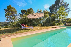 Ein Swimmingpool mit Liegestuhl und Sonnenschirm, umgeben von Bäumen.